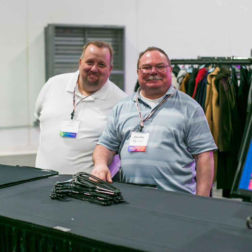 Two men smiling while volunteering at coat check